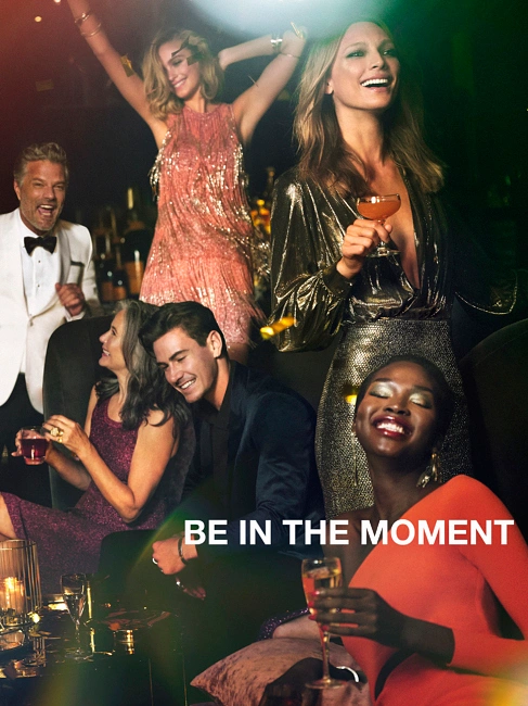 Group of smiling people in evening attire holding drinks at a party with warm lighting