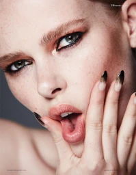 Close-up beauty portrait of a woman with freckles, dramatic eye makeup, and ombre almond nails resting against her chin.