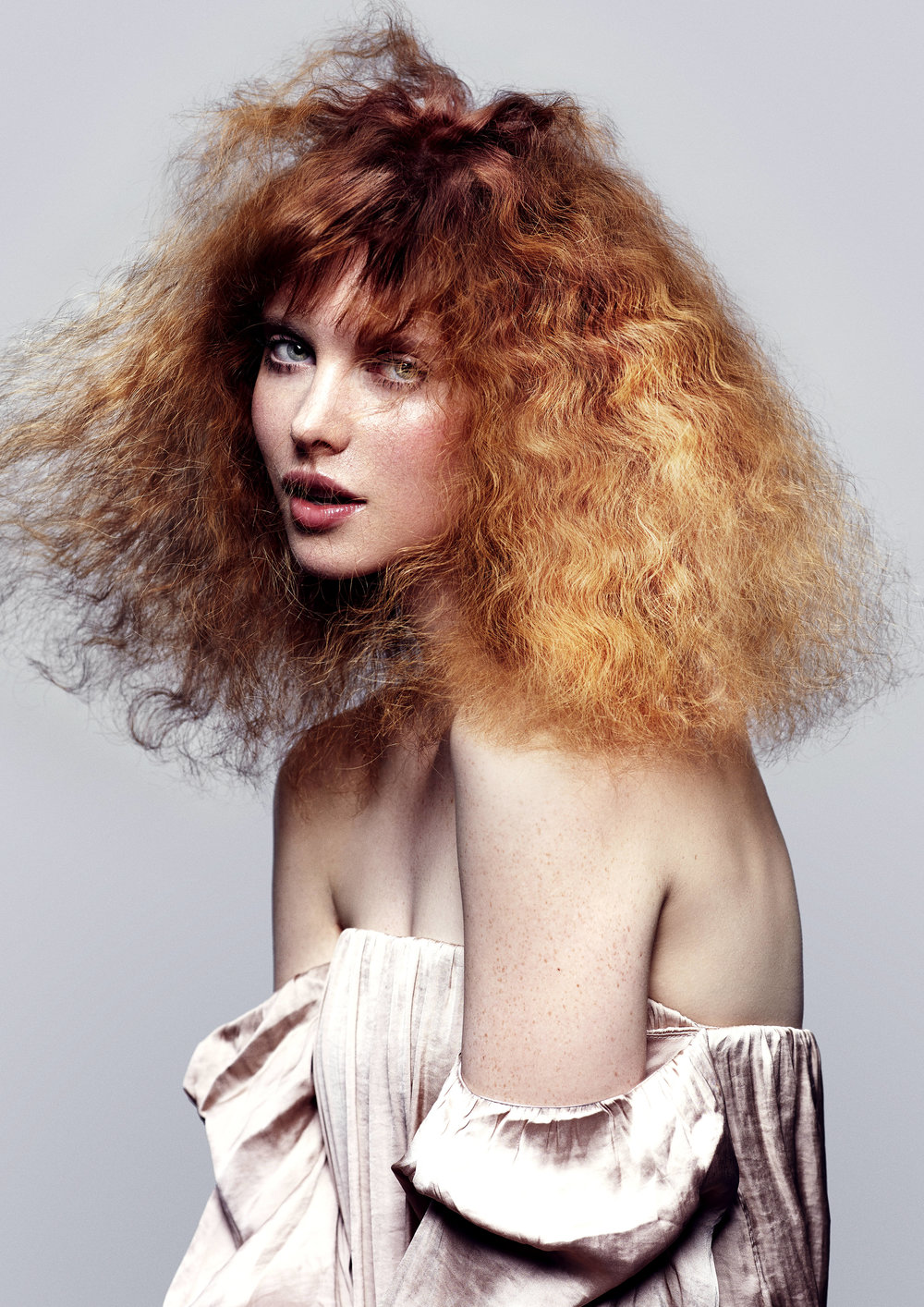 Headshot of a fair-skinned adult female with red hair and freckles wearing a pink gown against a light gray studio backdrop.