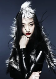 Close-up portrait of a woman with dramatic black and white hair styling wearing a black latex top against dark background