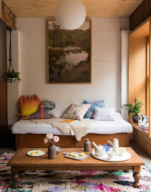 Interior of a bohemian-style living room with a daybed, throw pillows, a wooden coffee table with tableware, and a colourful patterned rug.