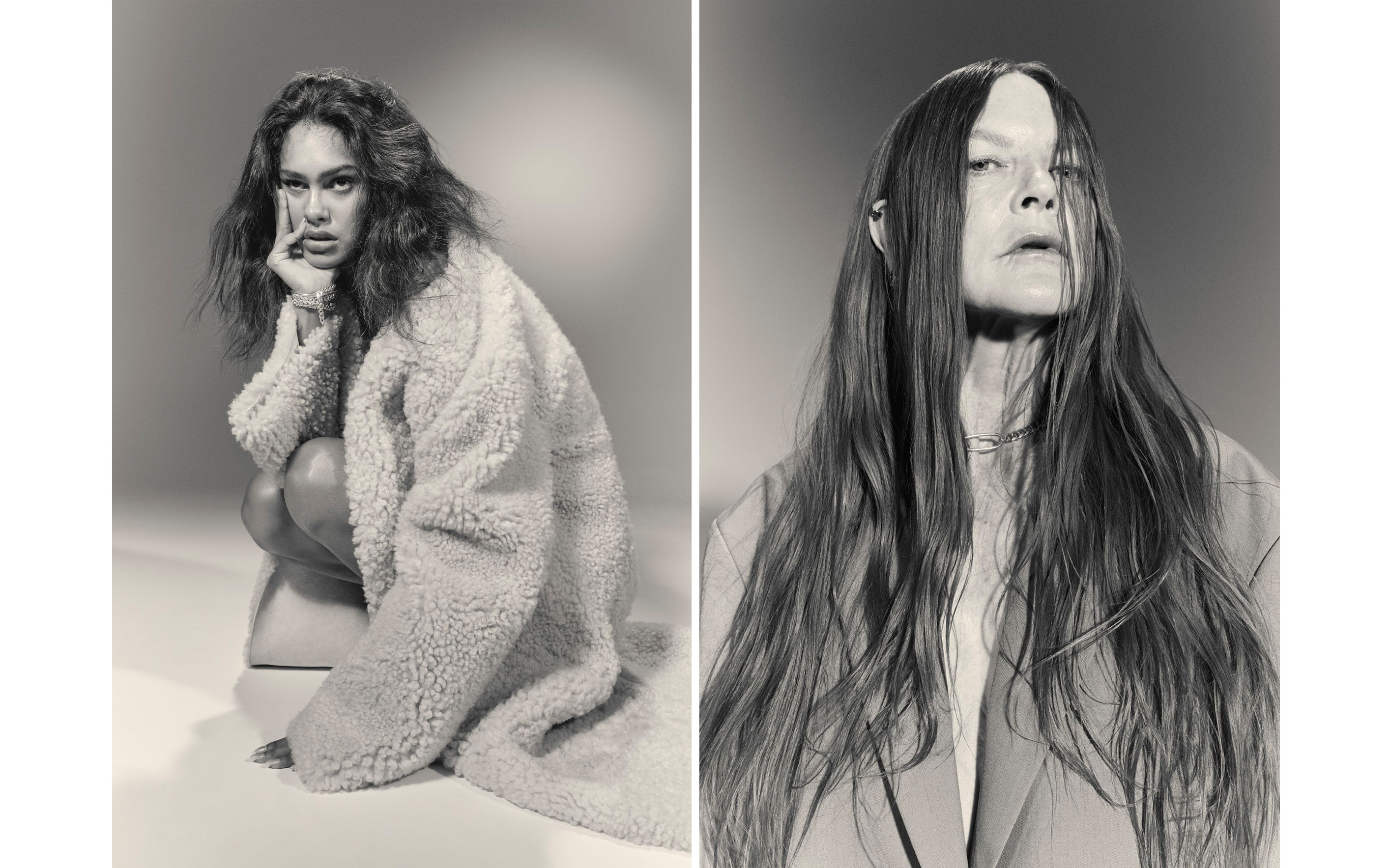 Two adult females pose in a black and white fashion shot in a studio. One wears a shaggy coat, the other a blazer.
