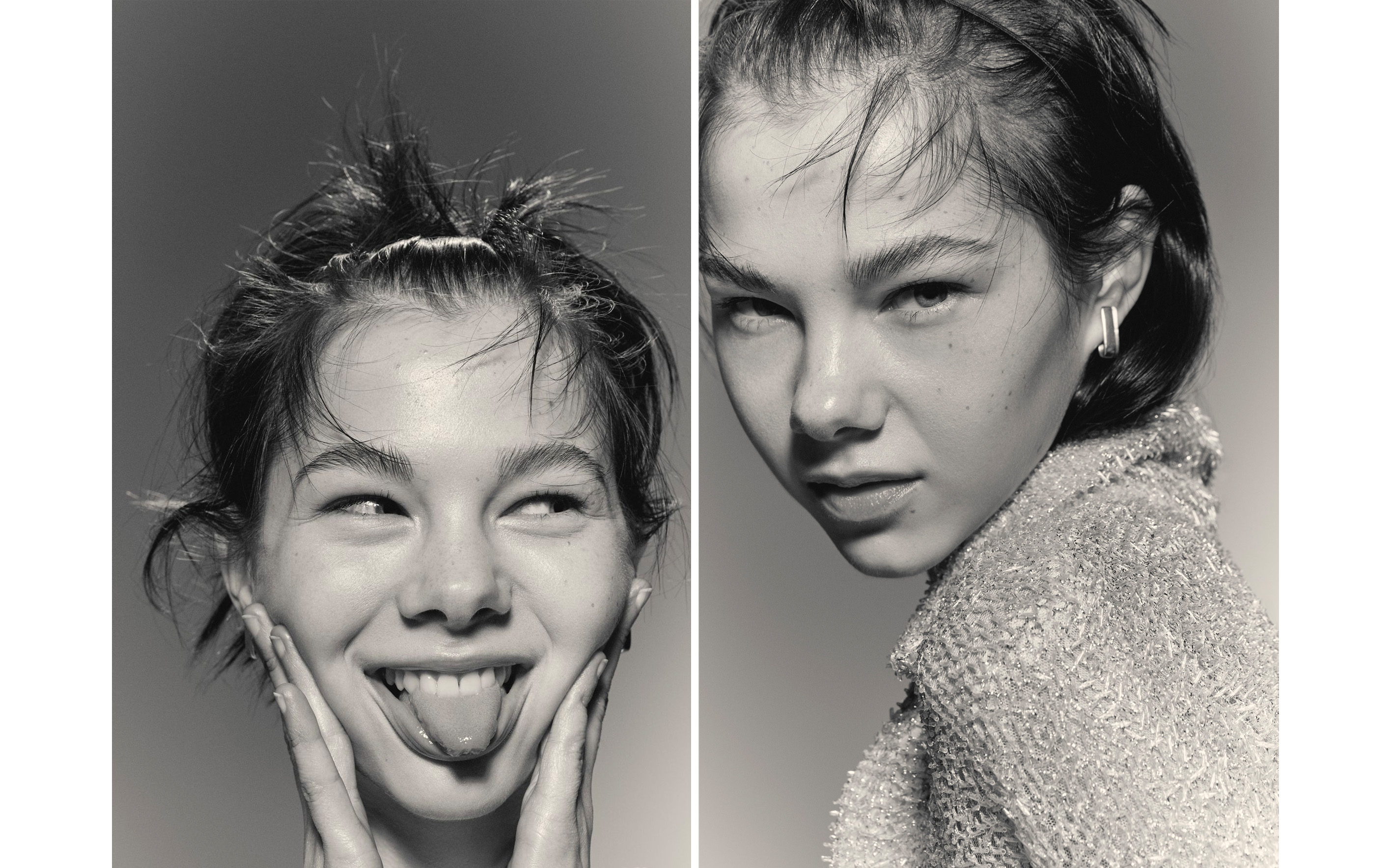 Monochromatic portrait of a young woman with playful expression, silver earrings, and textured light jacket against a grey background.