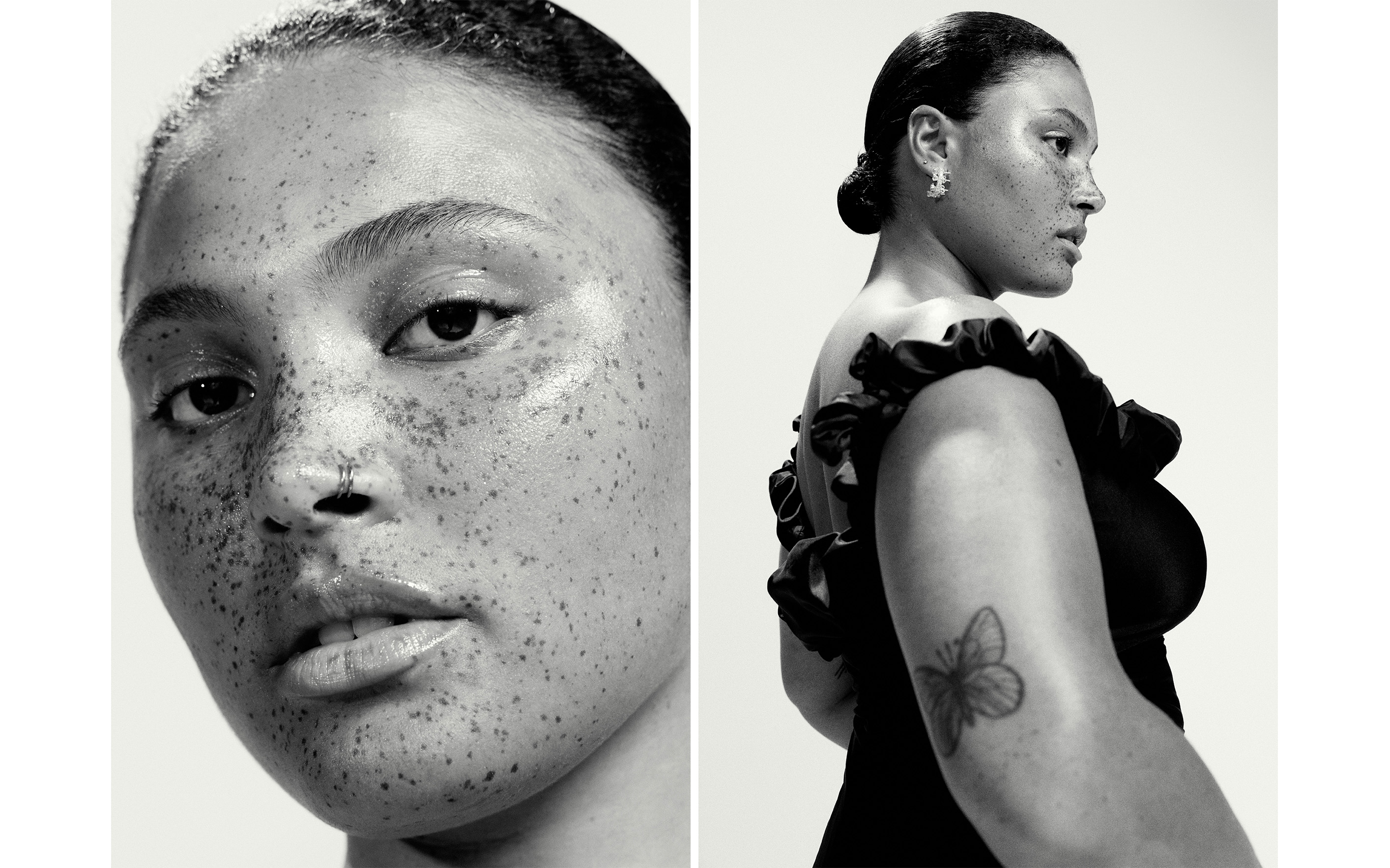 Black and white portrait of a woman with freckles and a nose ring, wearing an off-the-shoulder dress, against a neutral background.