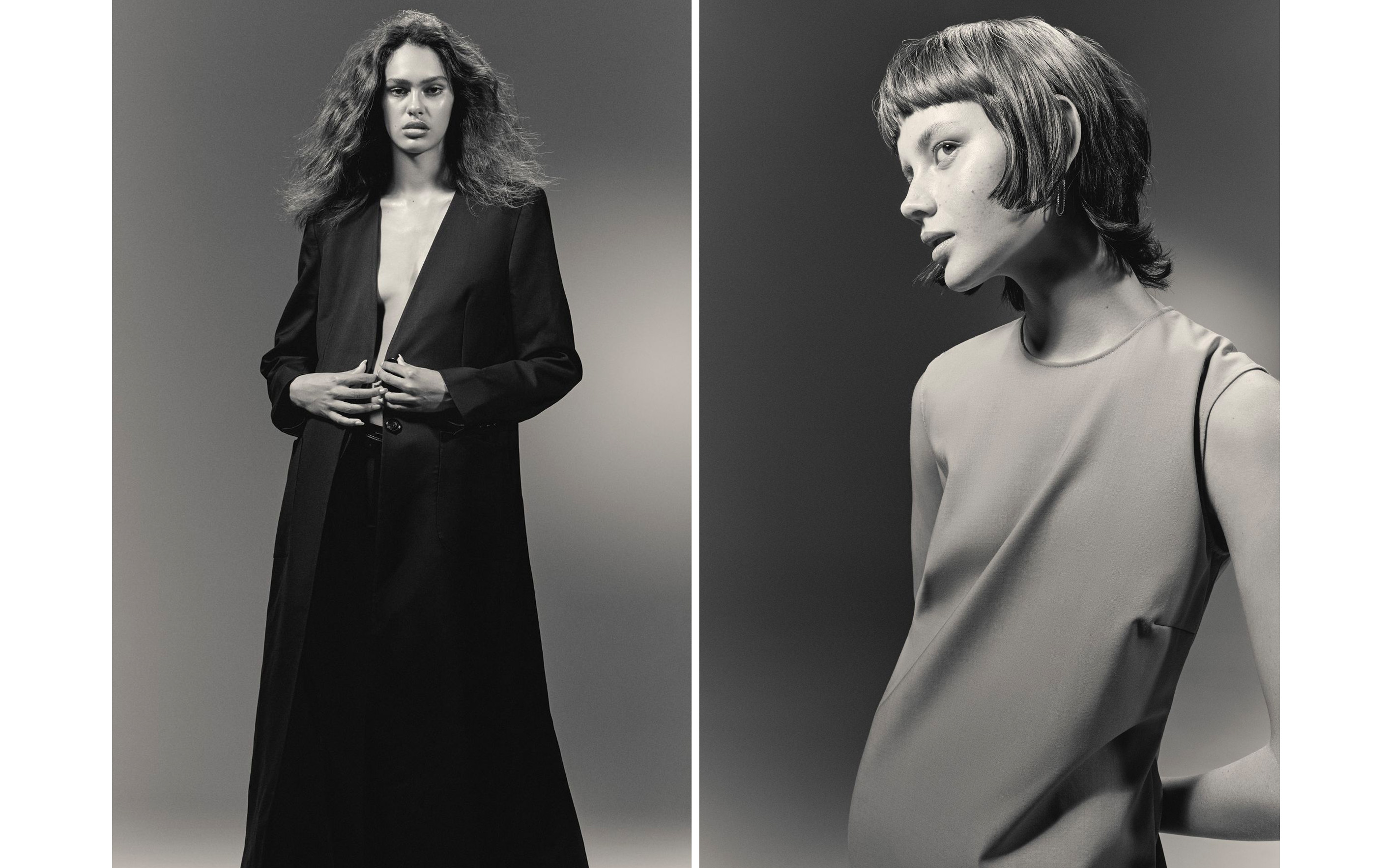 Two women in black and neutral dresses pose in a grayscale fashion editorial against a gray background under soft, diffused studio lighting.