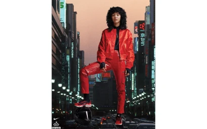 Model with curly dark hair wearing a bright red satin bomber jacket and matching red cargo trousers against a cityscape background