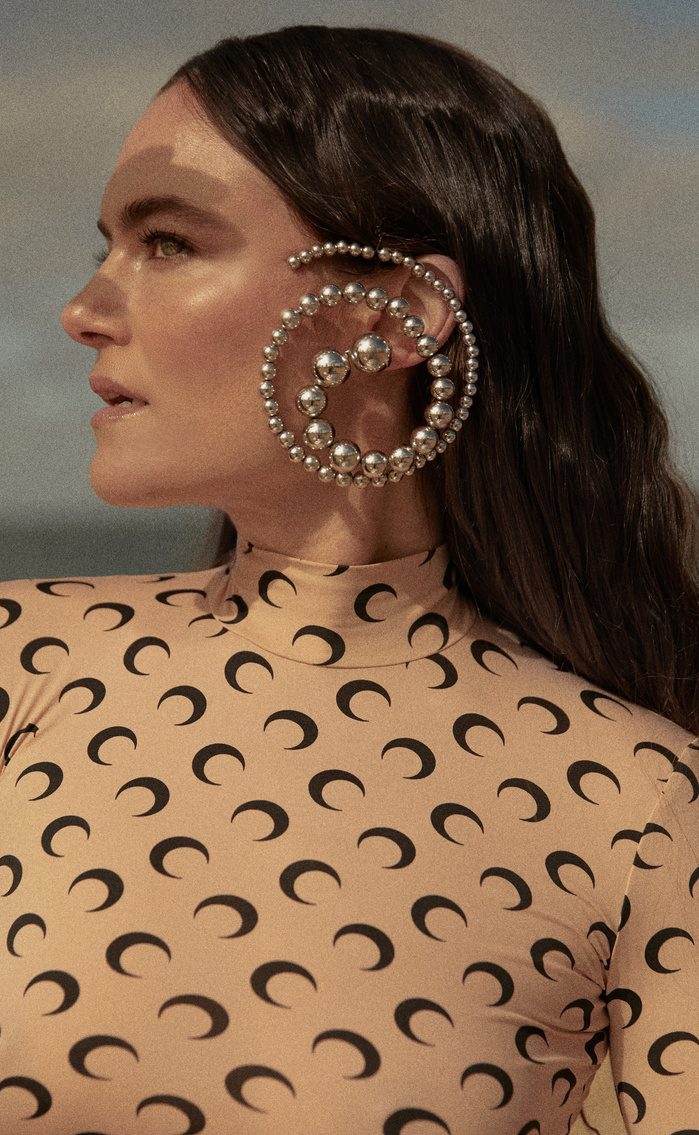 Woman wearing an oversize silver-tone beaded spiral ear cuff earring with crescent moon patterned tan turtleneck and a soft background.