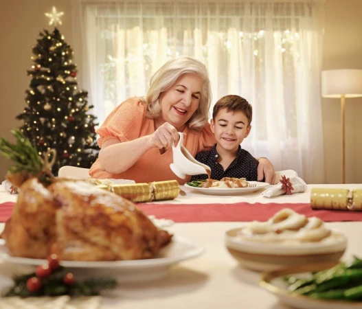 Grandmother and grandson share holiday meal together at a decorated table with a Christmas tree in the background at home.