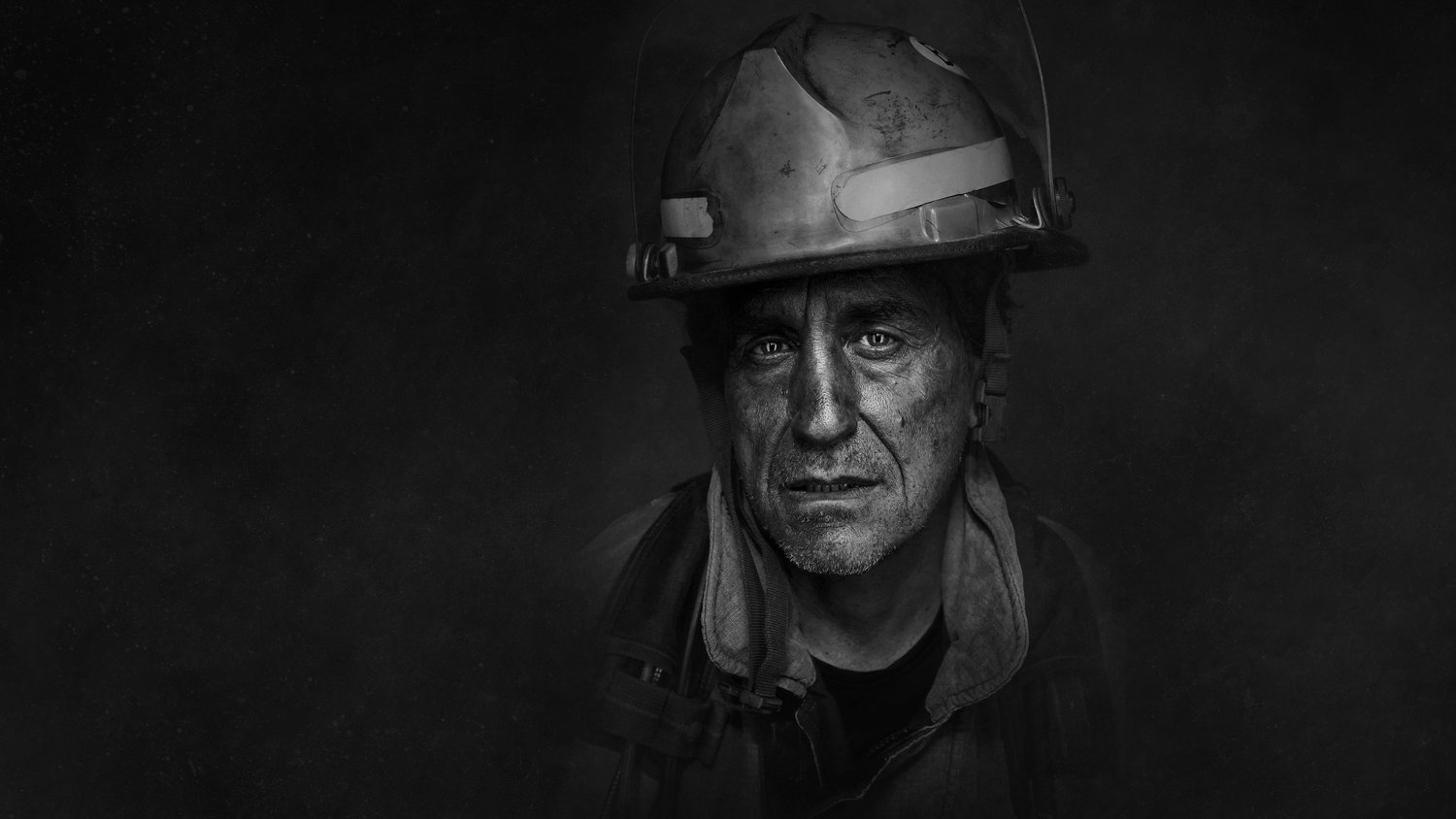 Monochrome portrait of a firefighter with a worn helmet, focused gaze, and textured skin against a dark, atmospheric background.