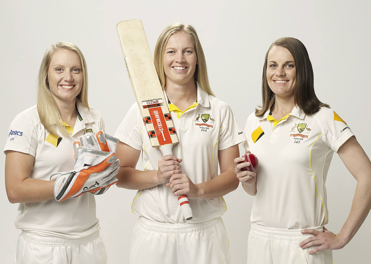 Three female cricket players pose in uniform with a bat, ball, and gloves against a white background, looking directly at the camera.