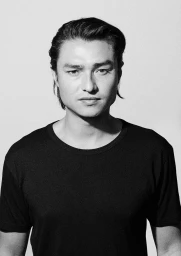 Portrait of a man with dark hair wearing a black t-shirt against a plain light background