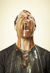 Man with sticky honey pouring down his face, mouth wide open, wearing a black t-shirt against a light seamless background