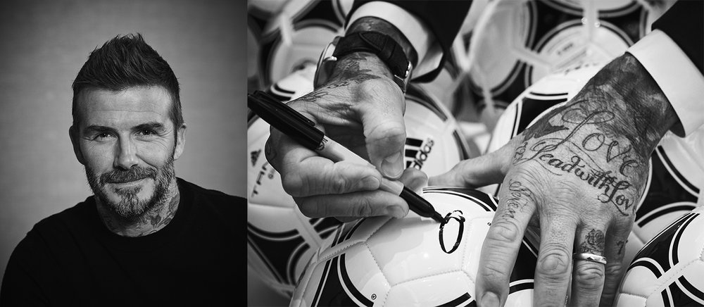 Black and white photo features a man signing a soccer ball, close-up of face and hands with tattoos against a soccer ball background.