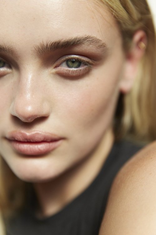 Close-up portrait of a blonde adult female looking at the camera. Her fair skin is visible along with her light green eyes and black top.