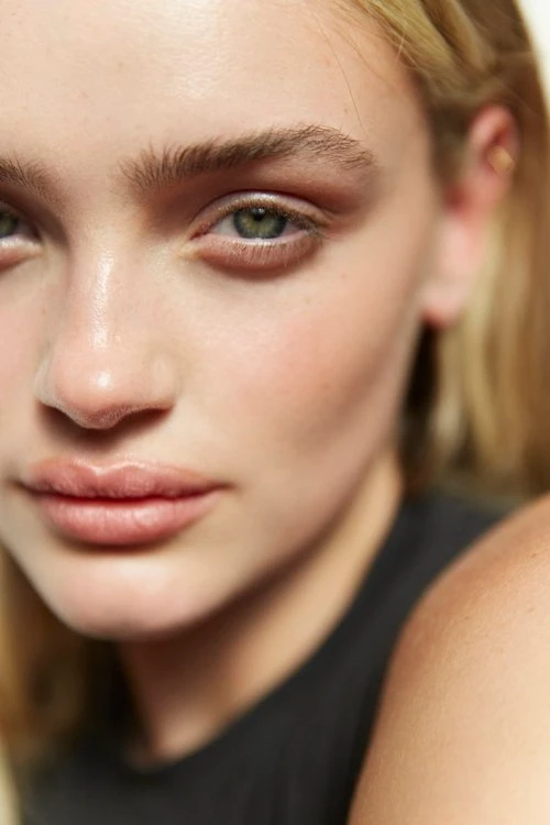 Close-up portrait of a woman with green eyes, natural makeup, and fair skin wearing a dark top in Melbourne.