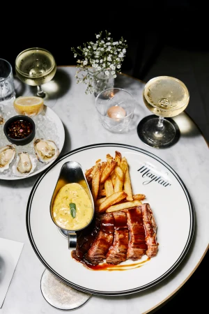Overhead shot: A plate of sliced steak with fries and sauce, set on a marble table with champagne and oysters, inviting food photography.