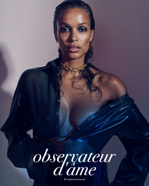 A dark-skinned female model poses in a shiny, wet-look shirt and gold choker against a soft pink-to-purple gradient background.