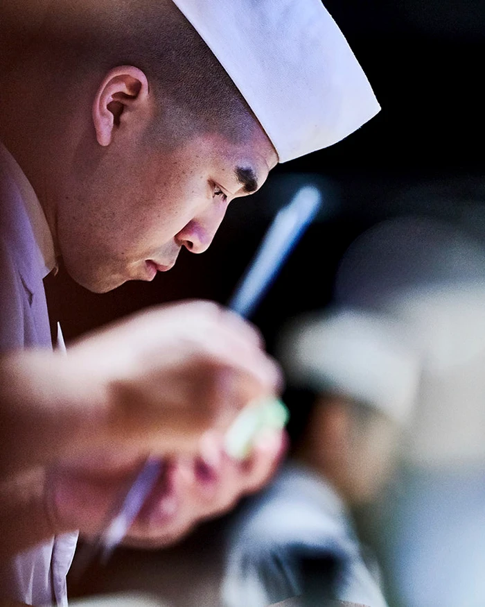 Close-up profile of a chef wearing a white toque and uniform focused on food preparation in Melbourne