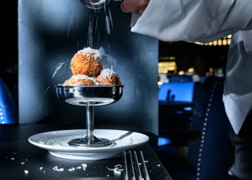 Chef grating cheese over stacked fried arancini balls in a metal footed bowl by Adrian Lander