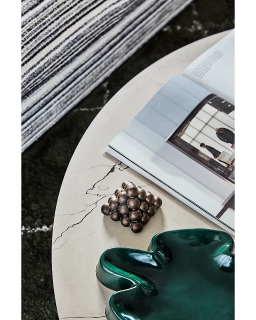 Close-up of a marble table displaying a magazine, decorative balls, and a green dish, set against a striped rug in an indoor setting.
