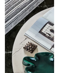 Close-up overhead view of a coffee table styled with a metallic sculpture, an open magazine, and a glossy green bowl.