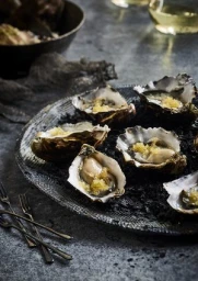 Freshly shucked oysters on a dark textured plate served with a golden garnish on a slate surface