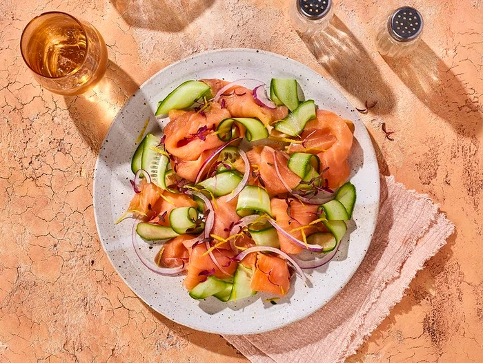 Overhead food photography of cured salmon salad with sliced cucumber and red onion on a ceramic plate.