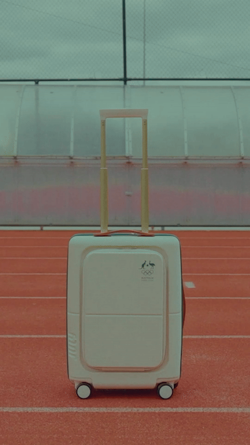 Roller suitcase on red track in an indoor training facility with a gray roof structure. Travel and sports concept.