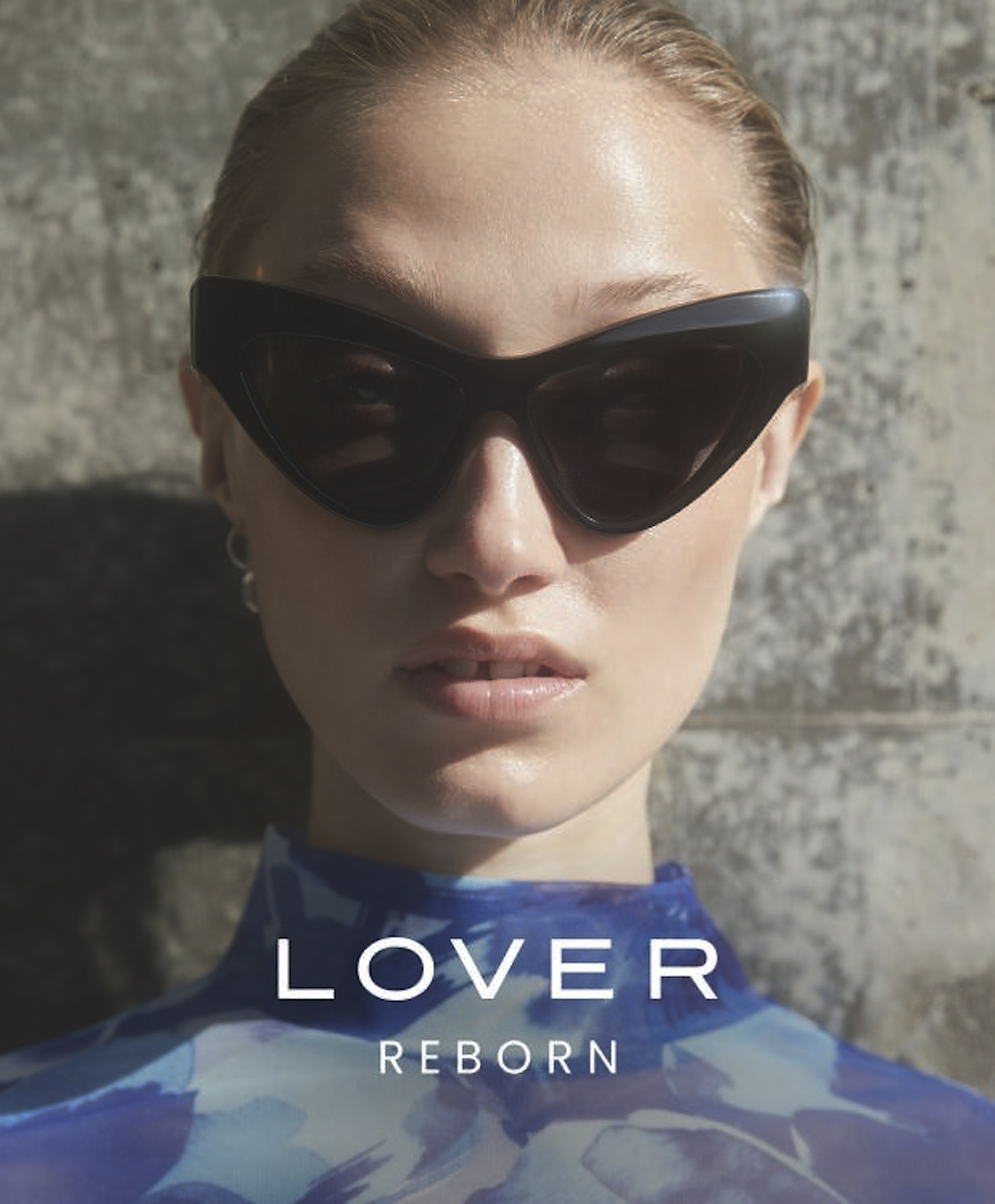 Close-up of a blonde woman wearing black sunglasses and a blue patterned top, posed against a neutral wall, with 