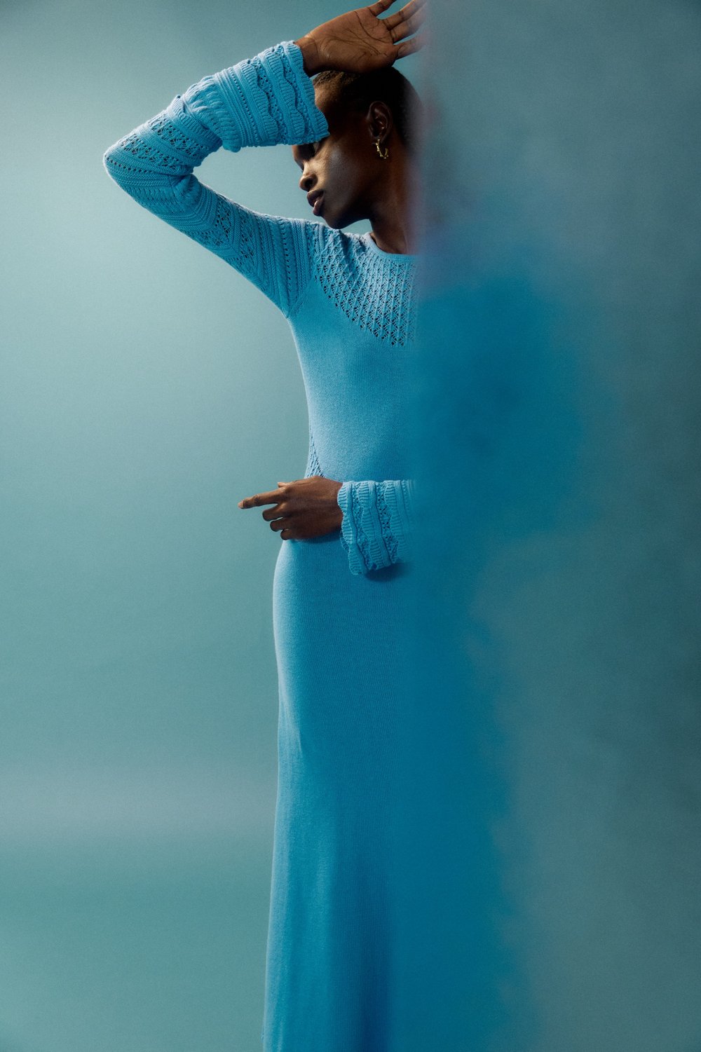 Black fashion model poses in a blue dress in a studio setting. The image features soft lighting, with a focus on the model's silhouette.