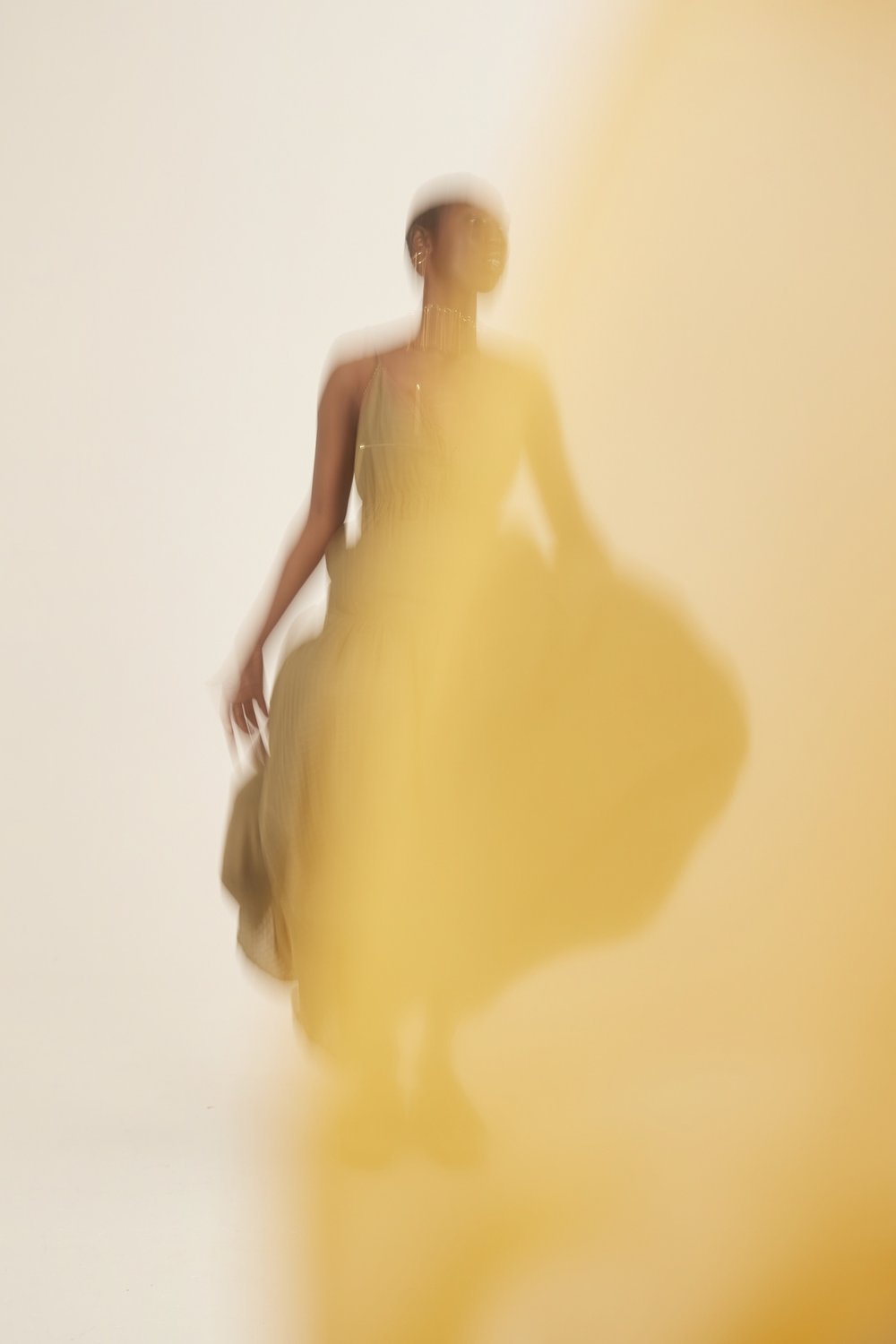 Abstract fashion photo featuring a female model in flowing yellow dress with motion blur, creating an artistic and dynamic visual effect.