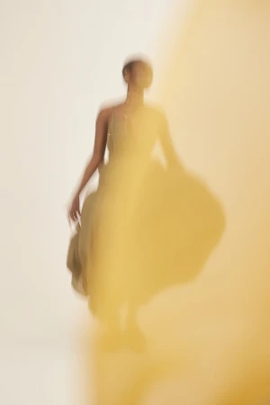 Abstract fashion photo featuring a female model in flowing yellow dress with motion blur, creating an artistic and dynamic visual effect.