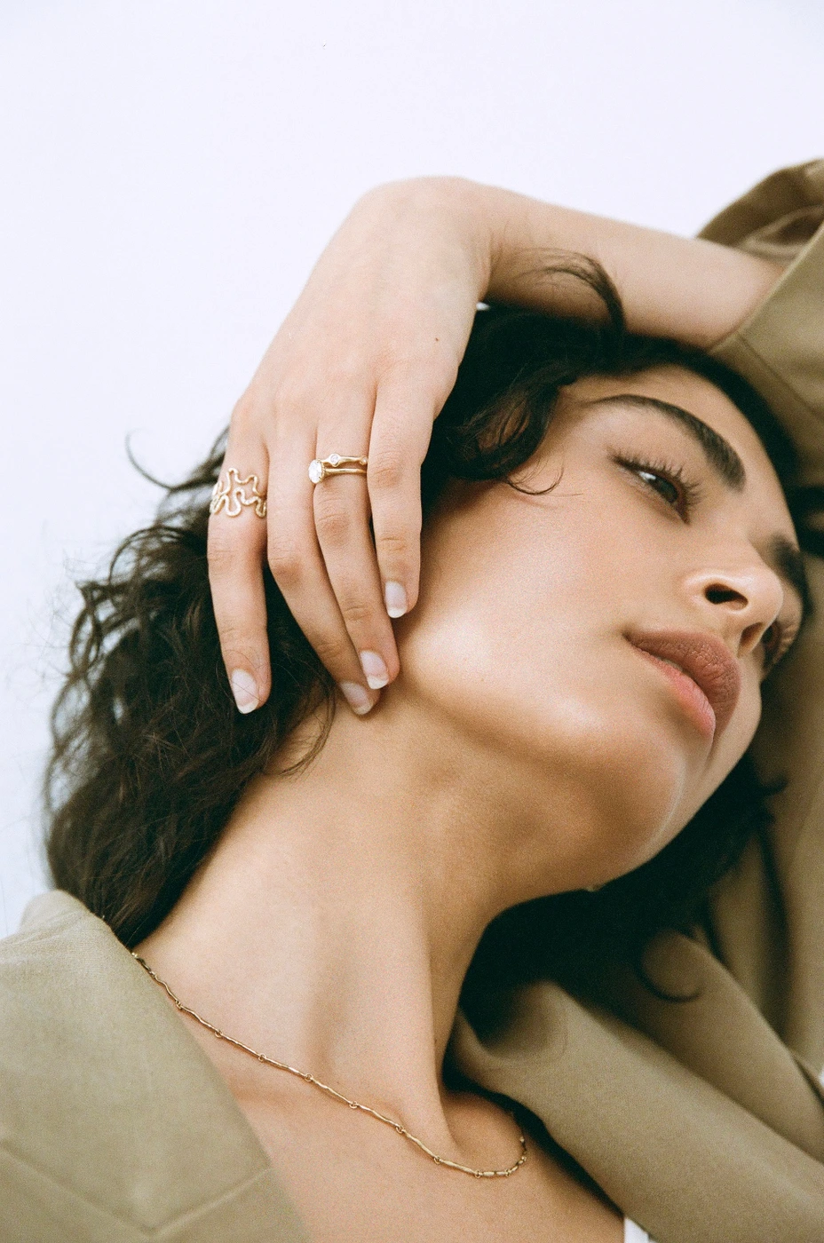 Close-up portrait of a woman wearing gold rings and a tan blazer against a plain white background by photographer Claire Wallman.