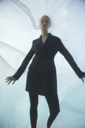 Model wearing a black double-breasted blazer and dark leggings against a draped white fabric background