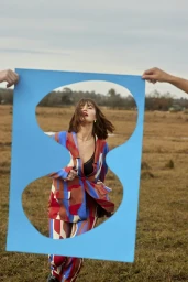 Woman in patterned suit holding blue cutout frame outdoors photographed by Claire Wallman
