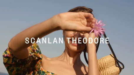 Woman holding a pink flower up to her face with a woven straw bag against a clear blue sky background