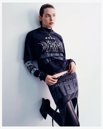 A female model in an indoor studio setting, leaning against a wall while wearing a stylish dark-wash matching skirt and top with knee-high boots.