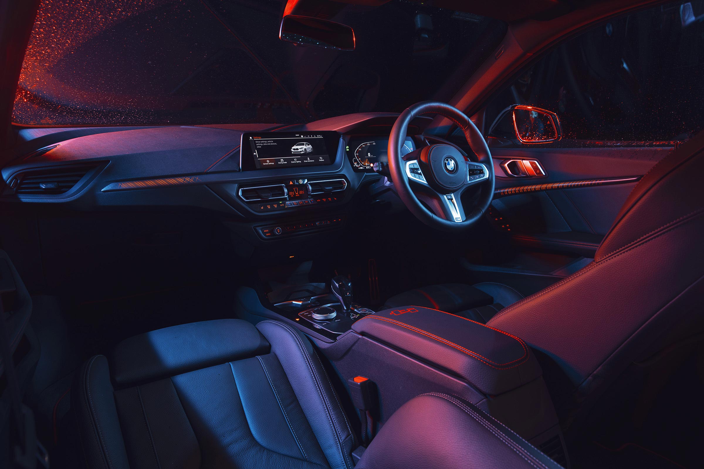 Car interior showcasing the steering wheel, dashboard, and seats, illuminated with blue and red ambient lighting.