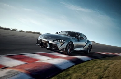 A silver sports car cornering on a racetrack with motion-blurred red and white curbs under a clear sky.