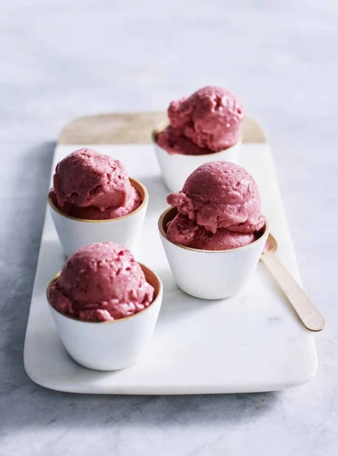 Four white bowls of reddish-pink ice cream on a marble surface with a wooden spoon on a bright background, food photography.