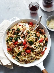 Spaghetti pasta with sausage, cherry tomatoes, spinach and parmesan in a white pan