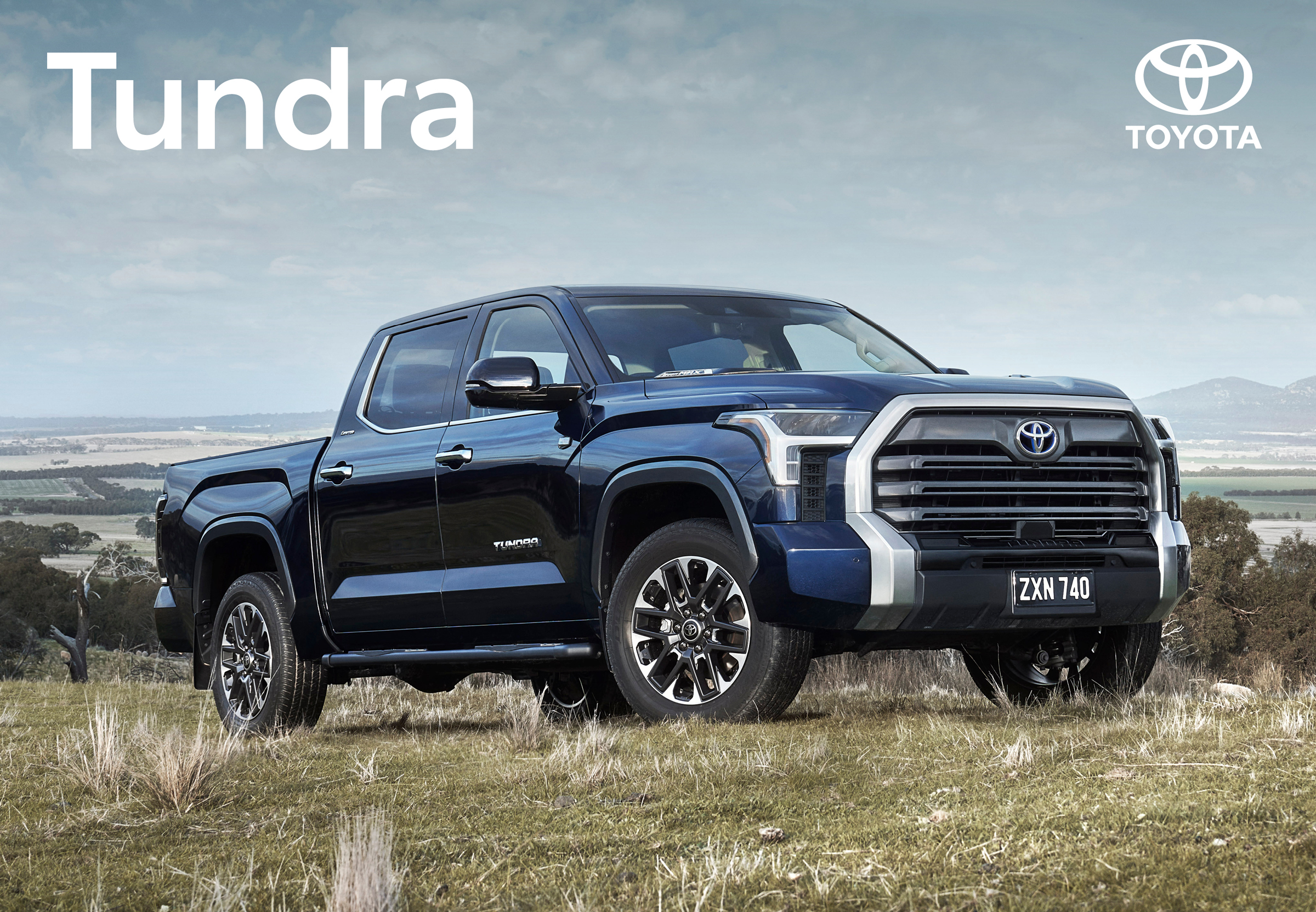 Dark blue Toyota Tundra pickup truck on a grassy hill with Toyota logo and Tundra text visible in a daylight outdoor shot.
