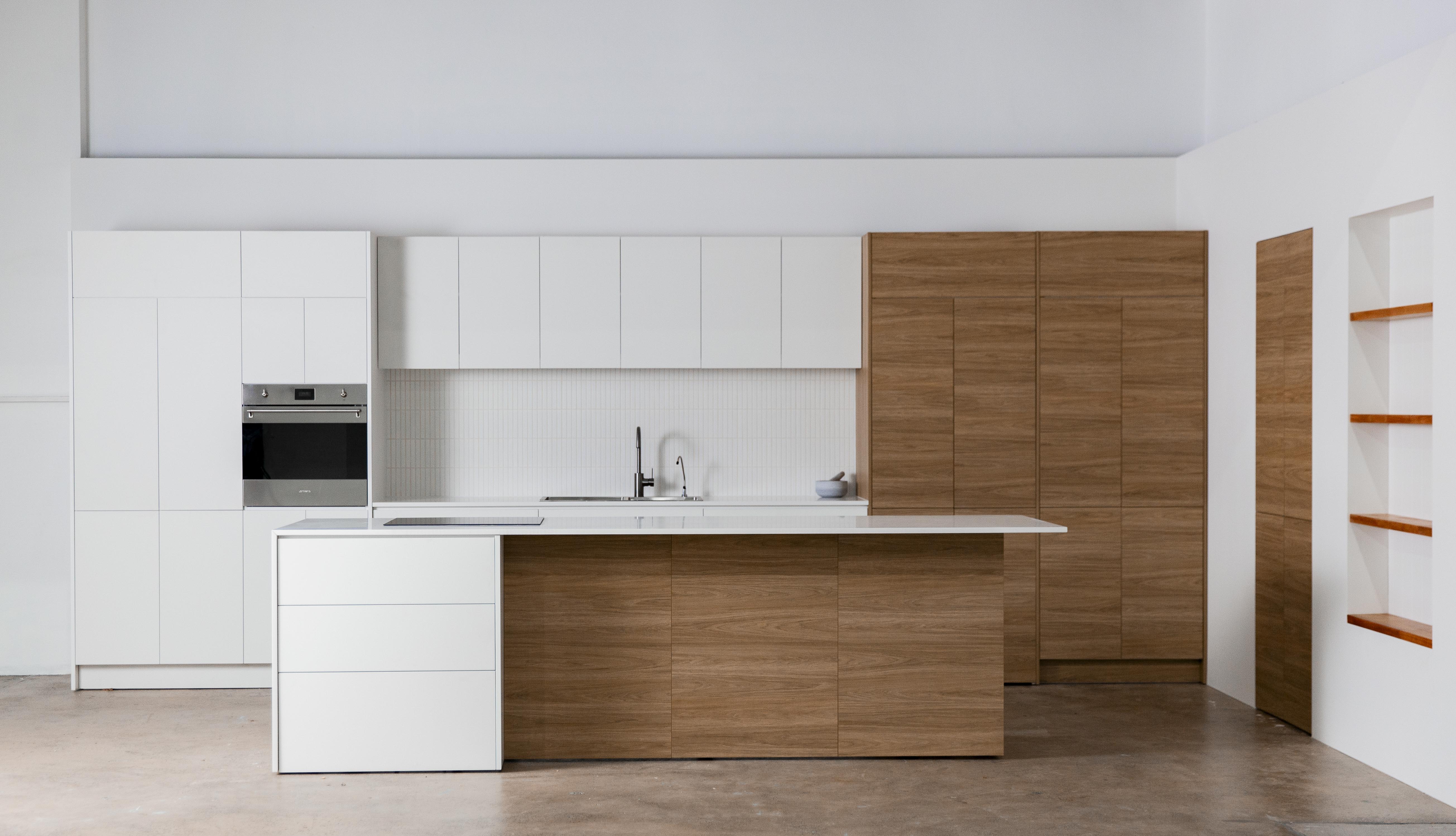 Bright, modern kitchen interior featuring white cabinets, wood island, stainless steel oven, and white tile backsplash.