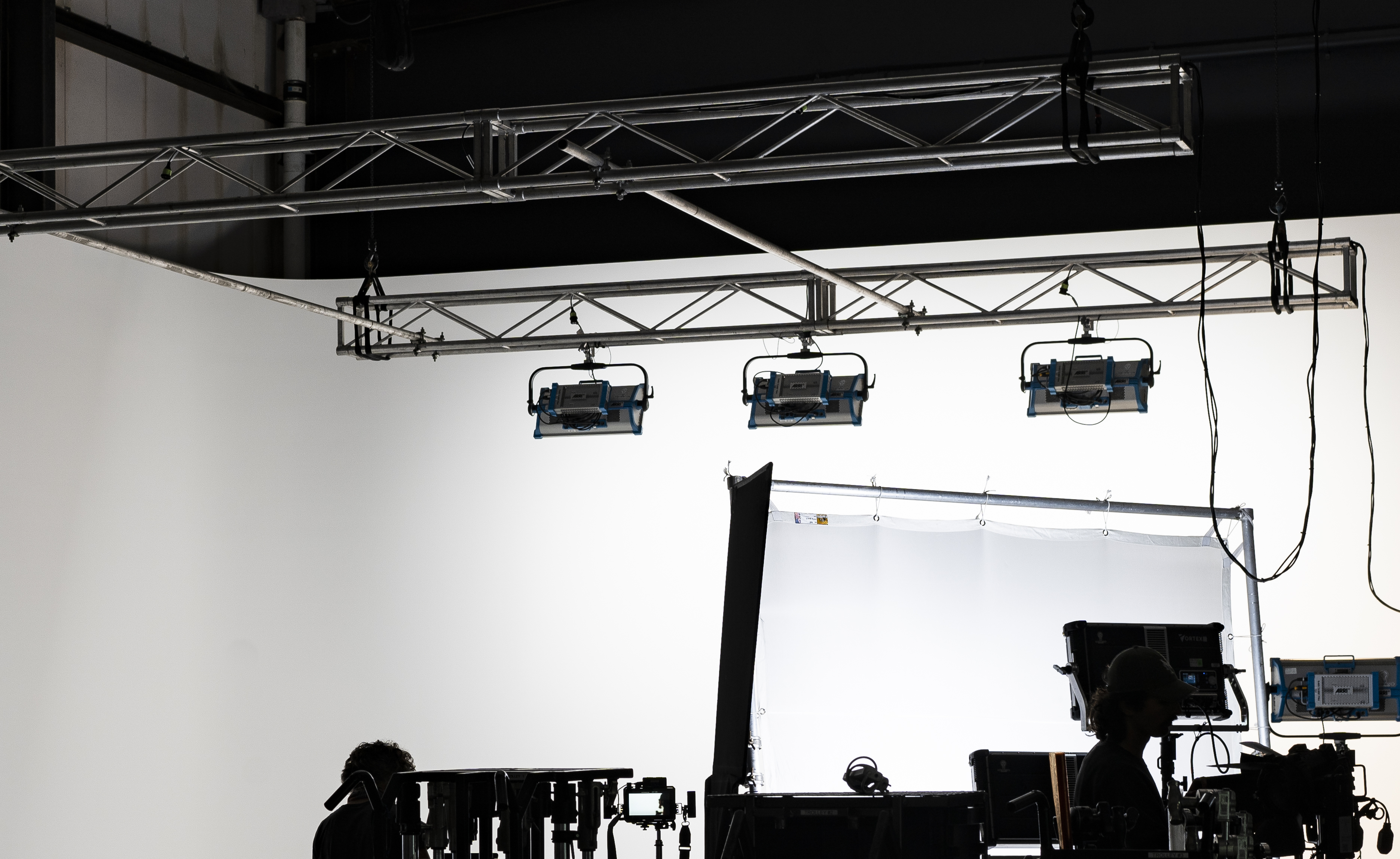 Bright photo studio interior showcasing lighting equipment, light screen, cameras, and studio monitors against a crisp white background.