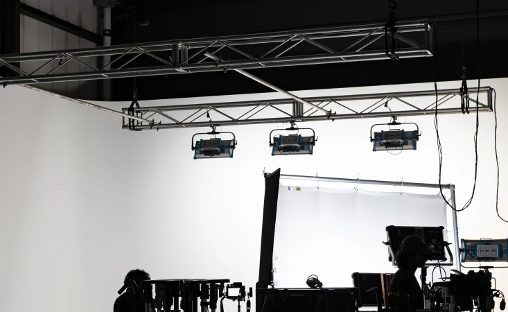 Bright photo studio interior showcasing lighting equipment, light screen, cameras, and studio monitors against a crisp white background.