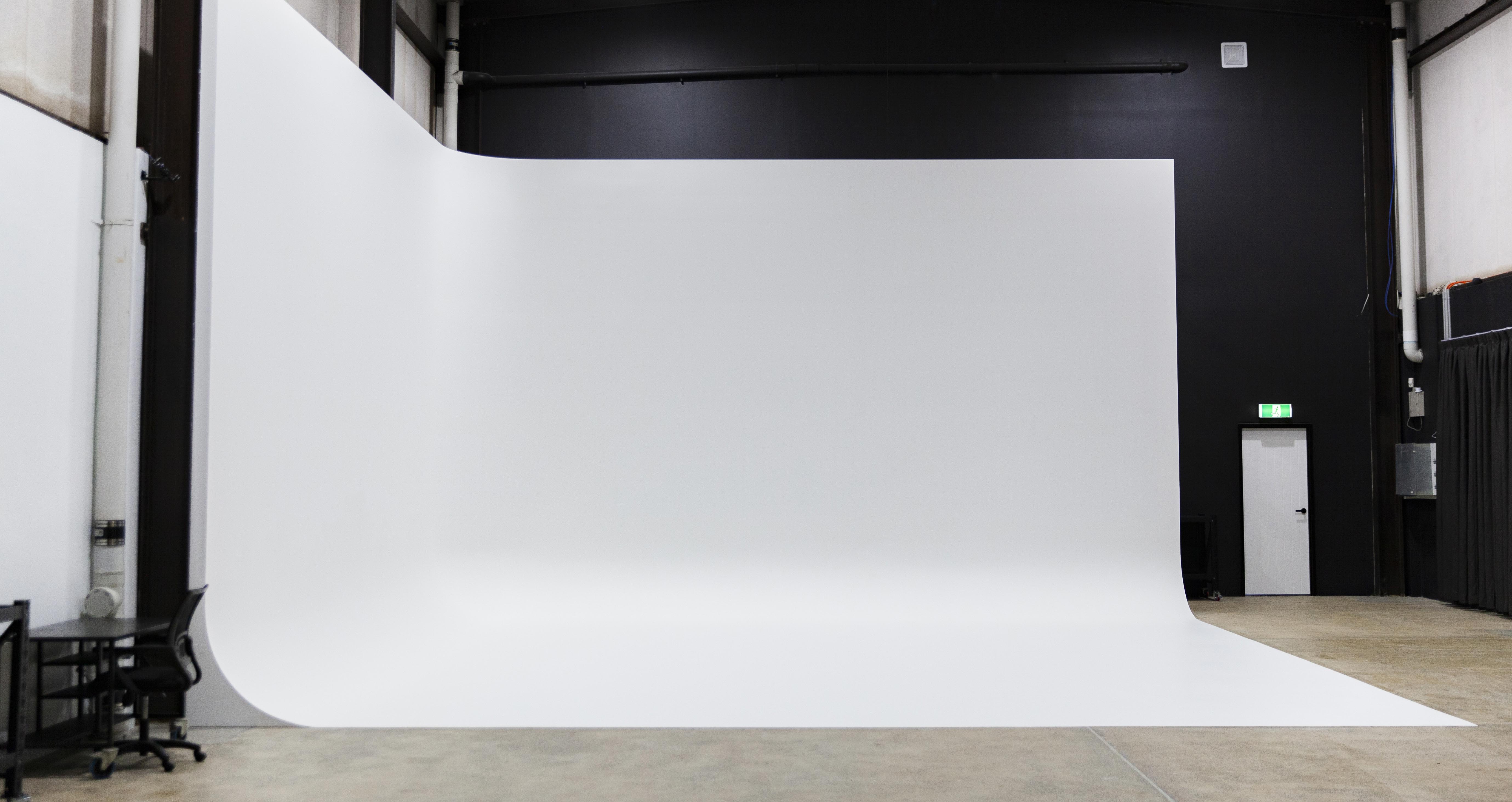 A large, curved white backdrop dominates the scene in a photography studio with black walls and a concrete floor with a minimal setup.