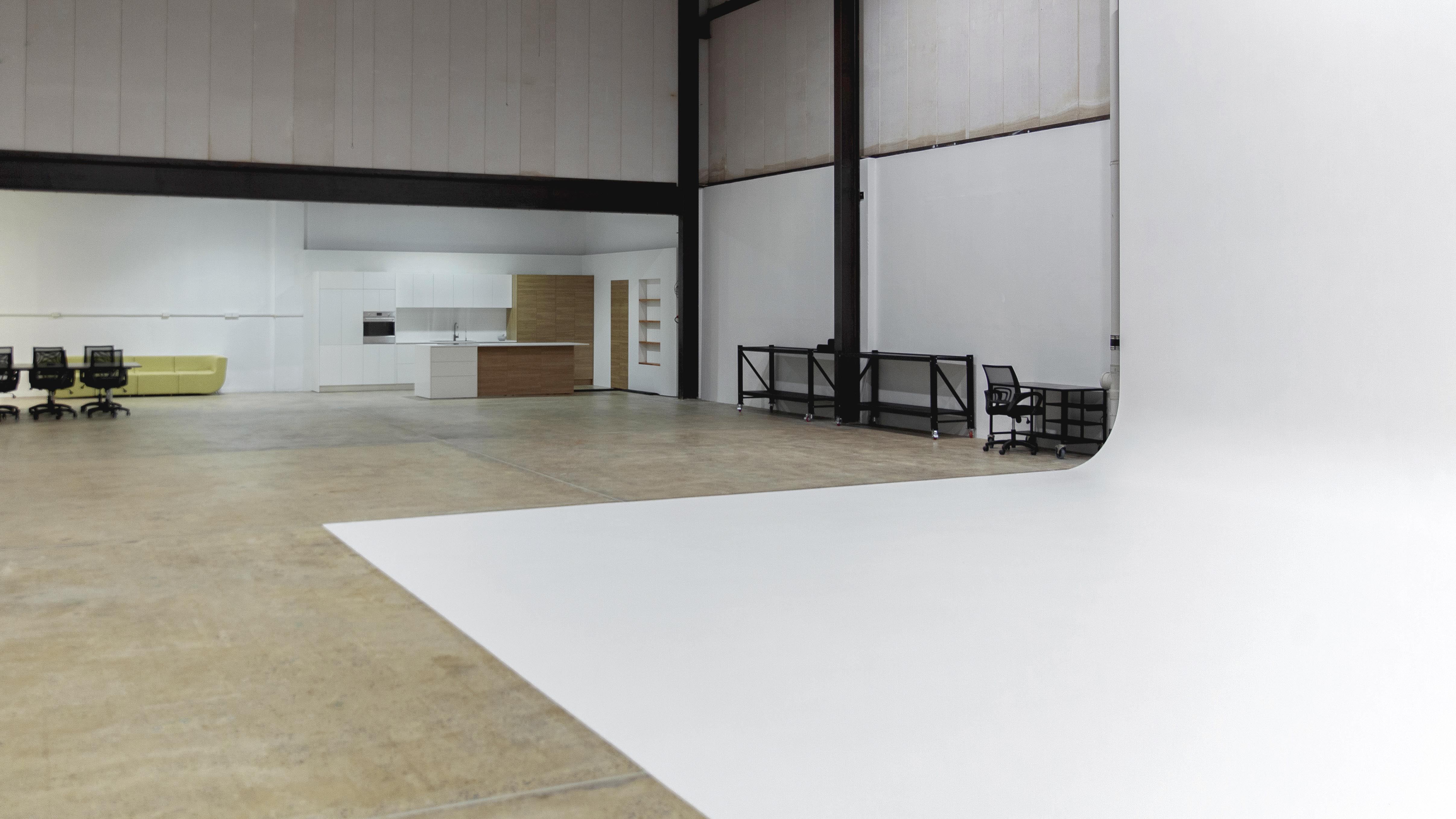Spacious photo studio interior with a seamless white backdrop, modern kitchen set, and office area. Good for architecture photography.