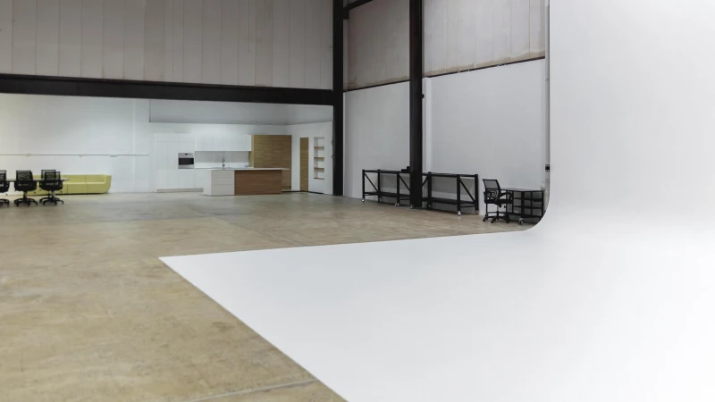 Spacious photo studio interior with a seamless white backdrop, modern kitchen set, and office area. Good for architecture photography.