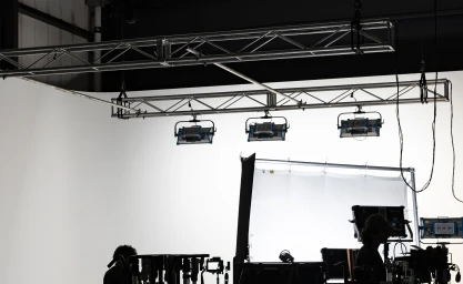 Silhouetted figures and professional lighting equipment inside a photo studio with a white cyclorama wall