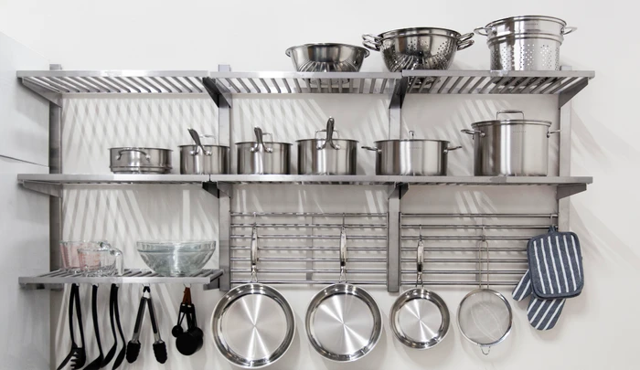 Stainless steel kitchen shelving unit mounted on a white wall displaying various pots, pans, and utensils by Studio Salt
